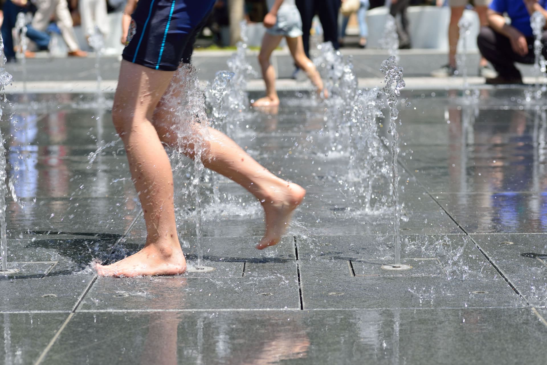 child playing in water fountain in the heat